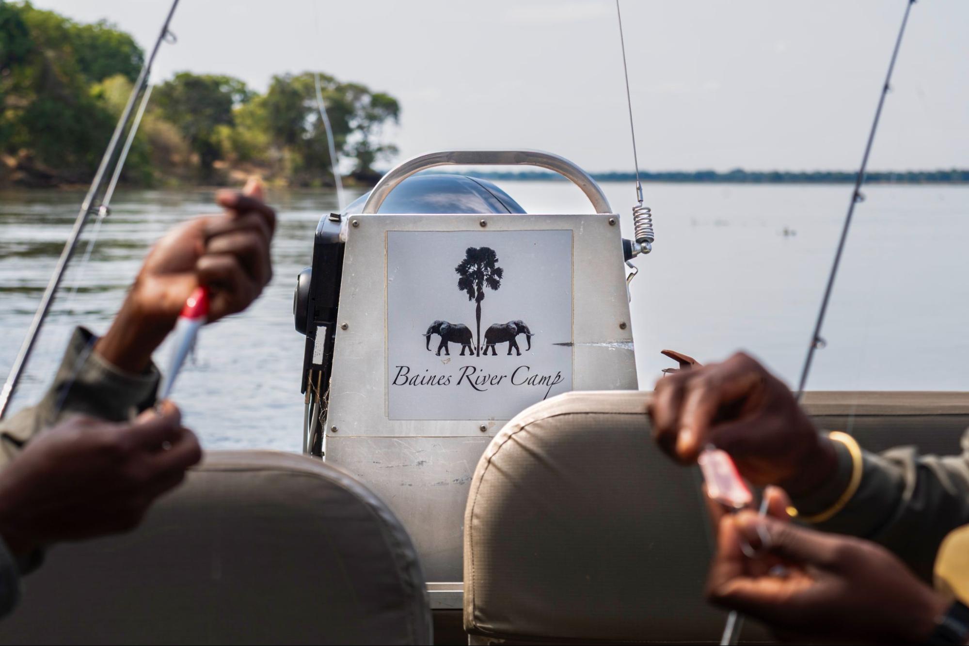 Angler holding a lure beside a Baines River Camp boat on the Zambezi